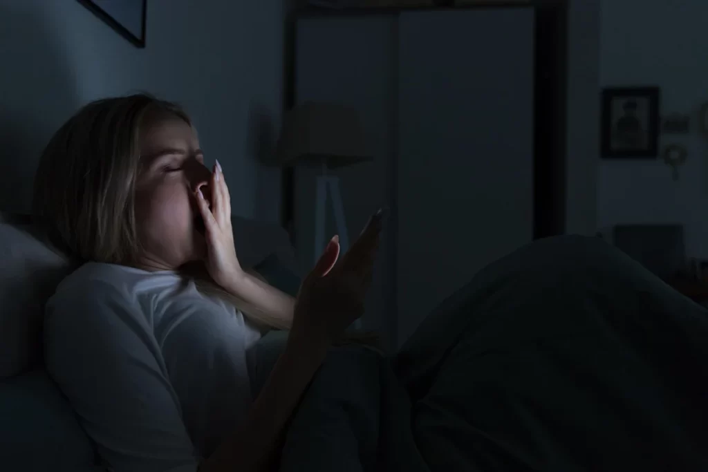 sleepy woman lying in bed using smartphone.