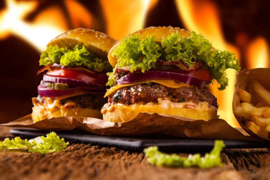 Two hamburgers with fire in the background.