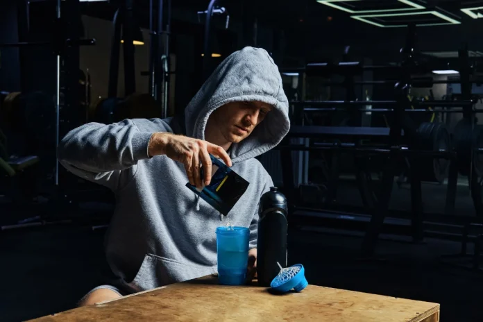 Athlete pouring energy protein (earth energy supplements)powder in his drink in the gym.